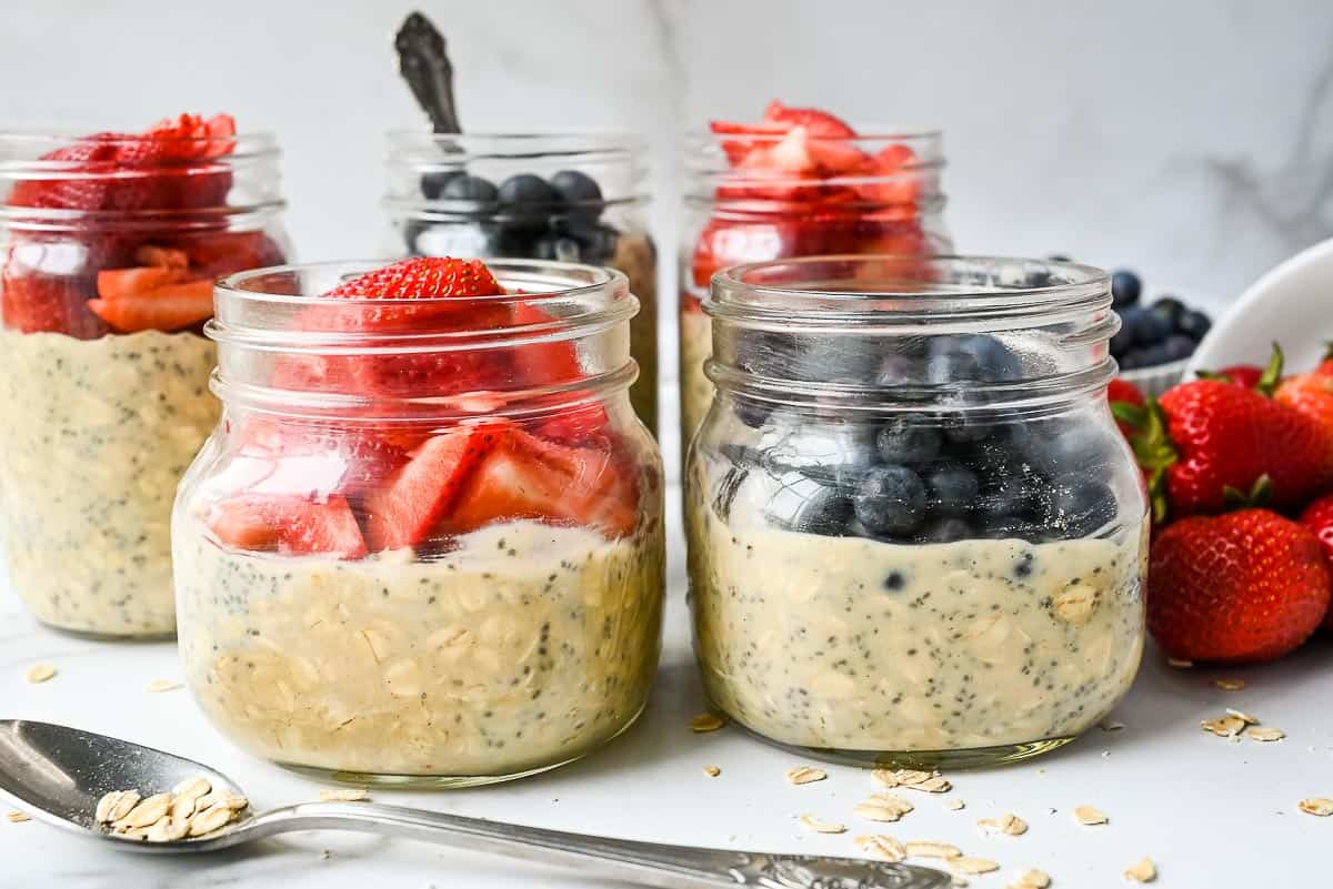 two jars of overnight oats with protein topped with strawberries and blueberries