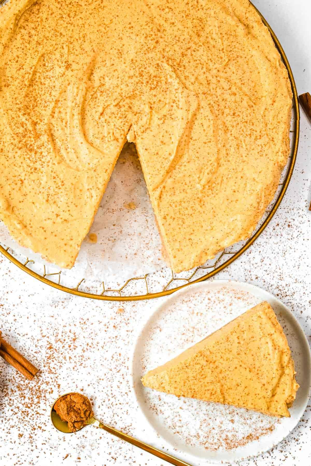 slice of pumpkin cheesecake next to full cheesecake on a white background.