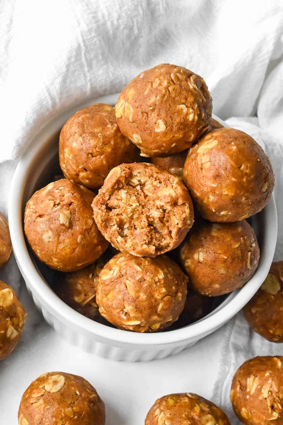bowl of pumpkin protein balls in a white dish on a white background with a bite shot.
