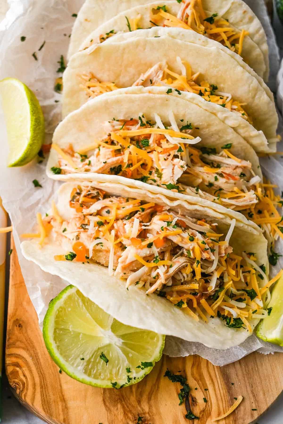 chicken tacos lined up on a wooden board with lime