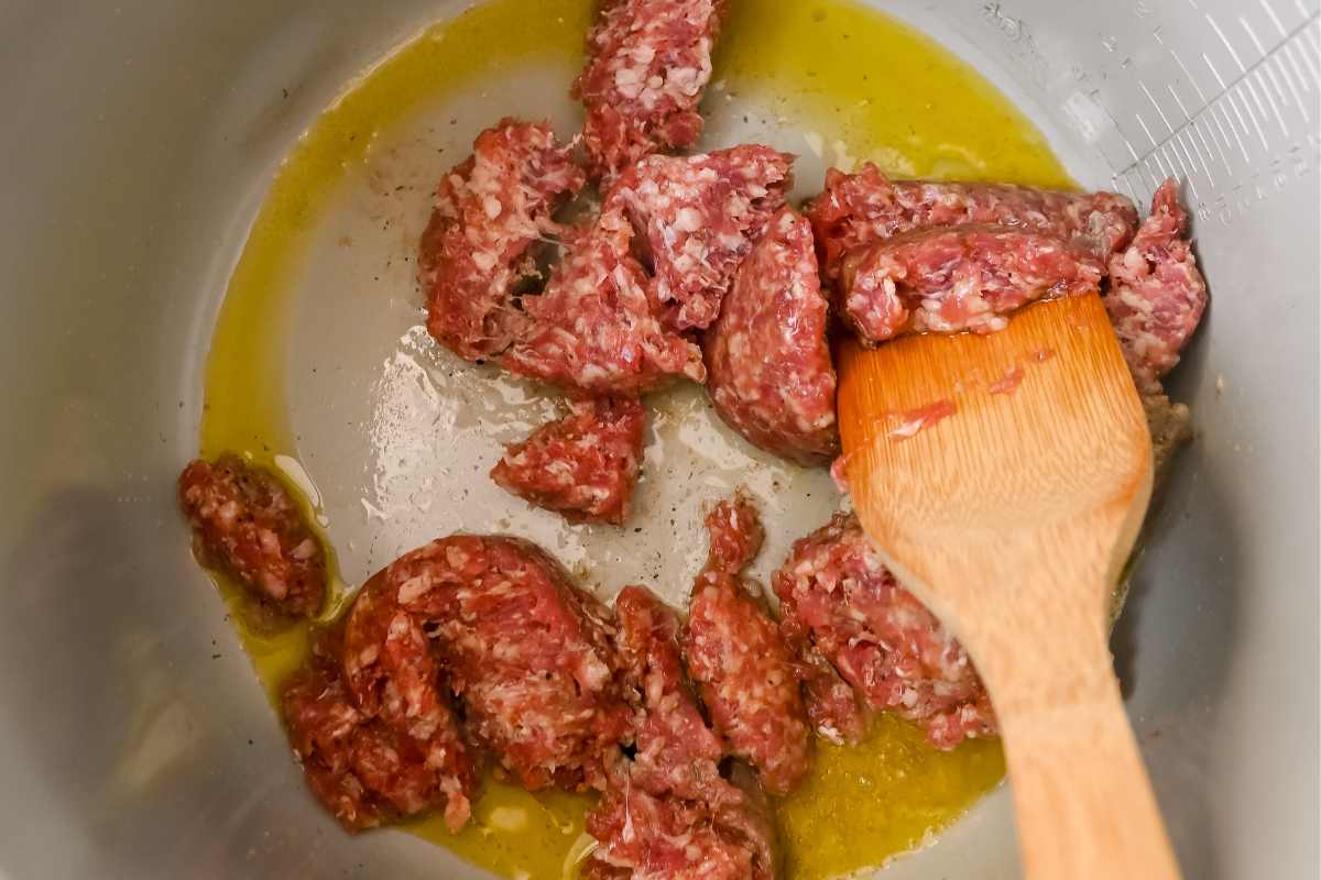 sausage and oil cooking in an instant pot with a wooden spatula.