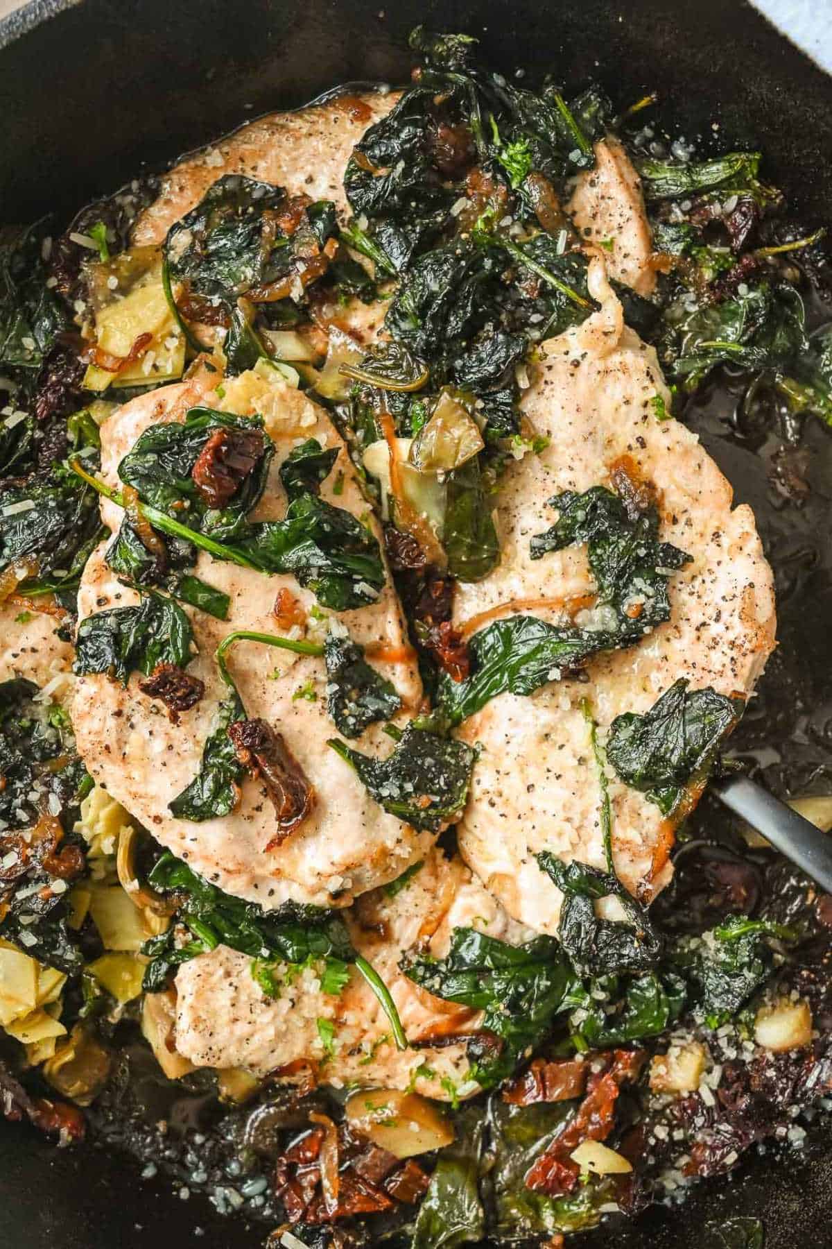 close up shot of two chicken pieces topped with spinach in a cast iron skillet.