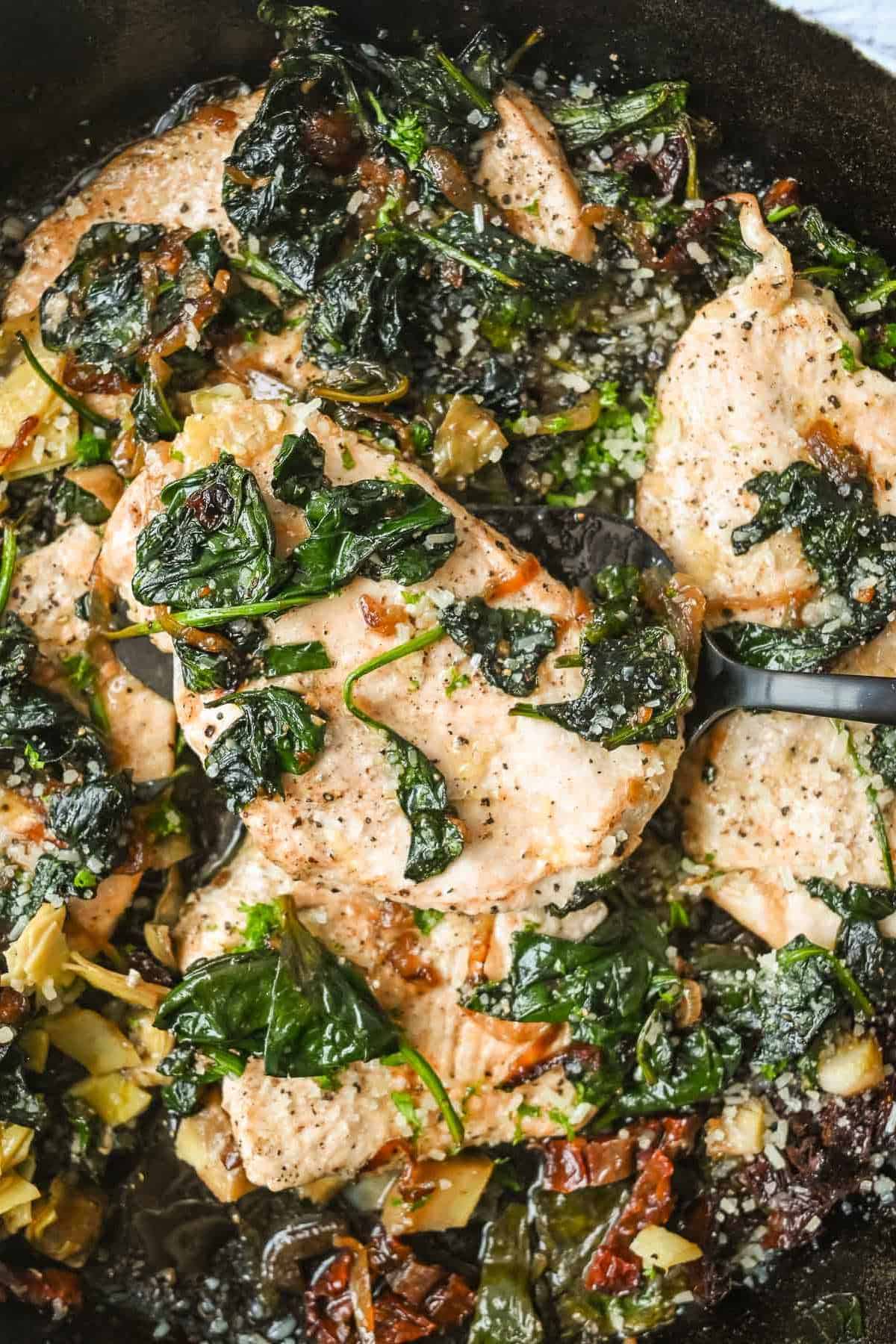 close up shot of chicken topped with spinach in a cast iron skillet.