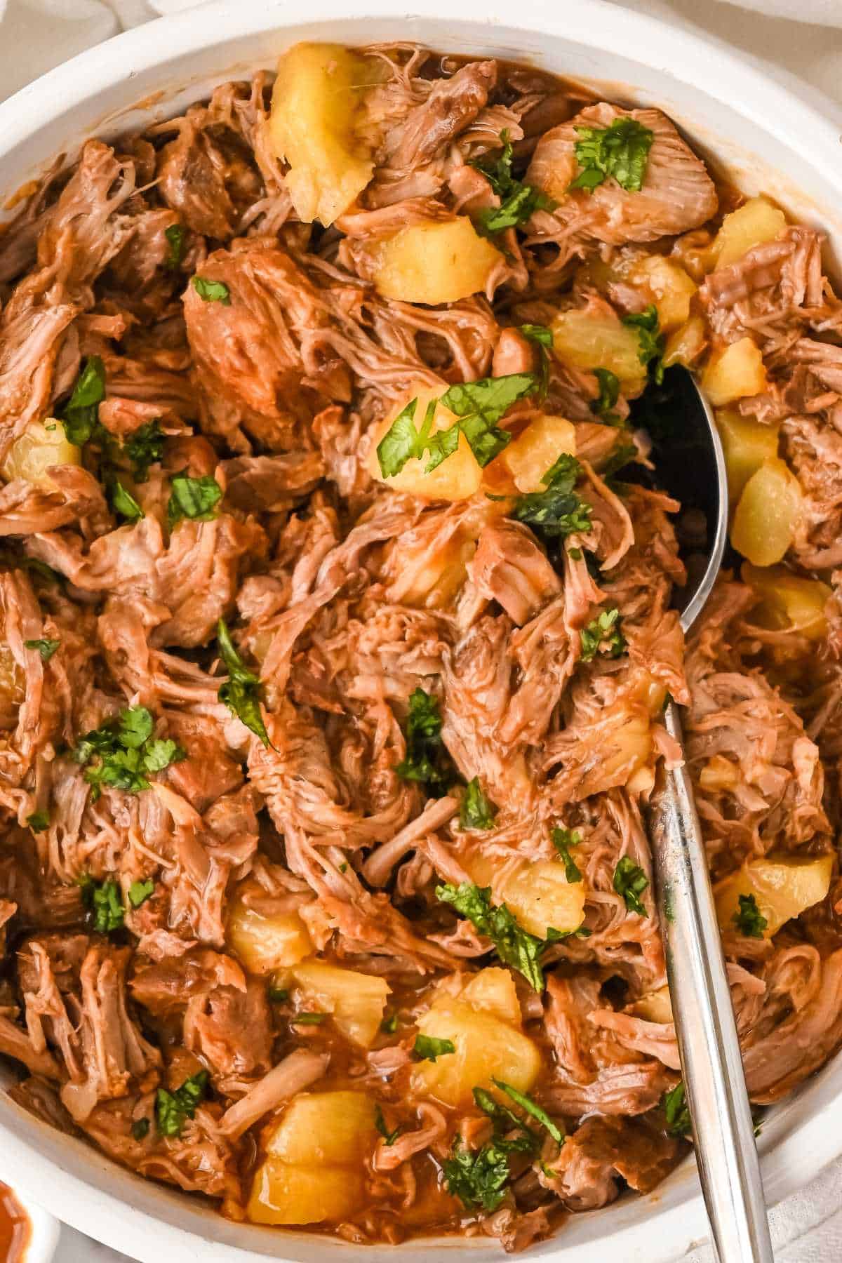 close up of pineapple pulled pork in a white bowl with a spoon topped with cilantro.