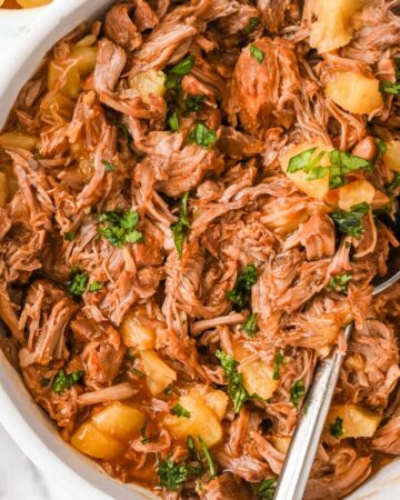 close up view of pineapple pulled pork topped with cilantro with a spoon in a white bowl.