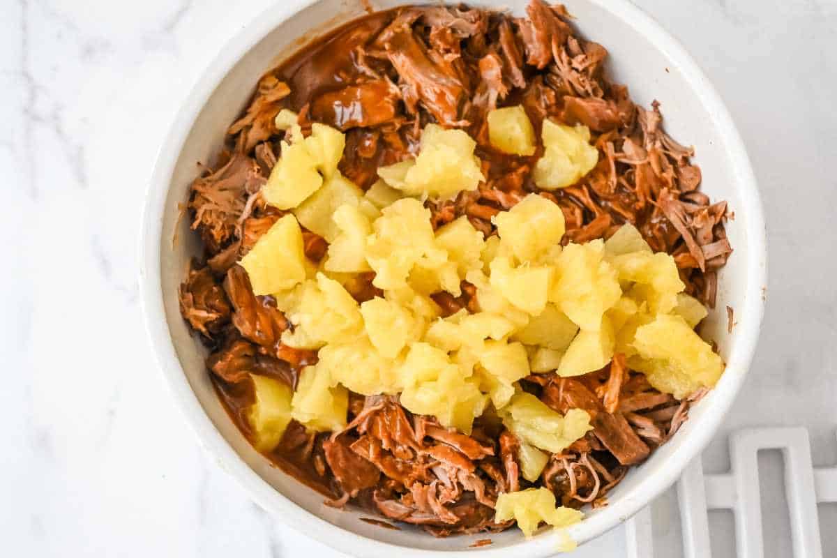 pineapple pulled pork with pineapple chunks in a white bowl.