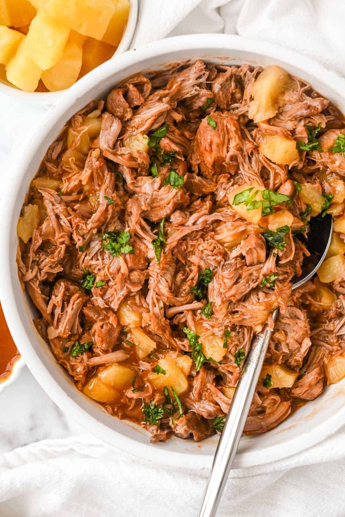 top view of pineapple pulled pork on a white background in a white bowl with pineapple in a bowl next to it.