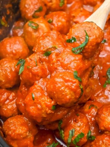 close up shot of meatballs in a crock pot with a wooden spoon.