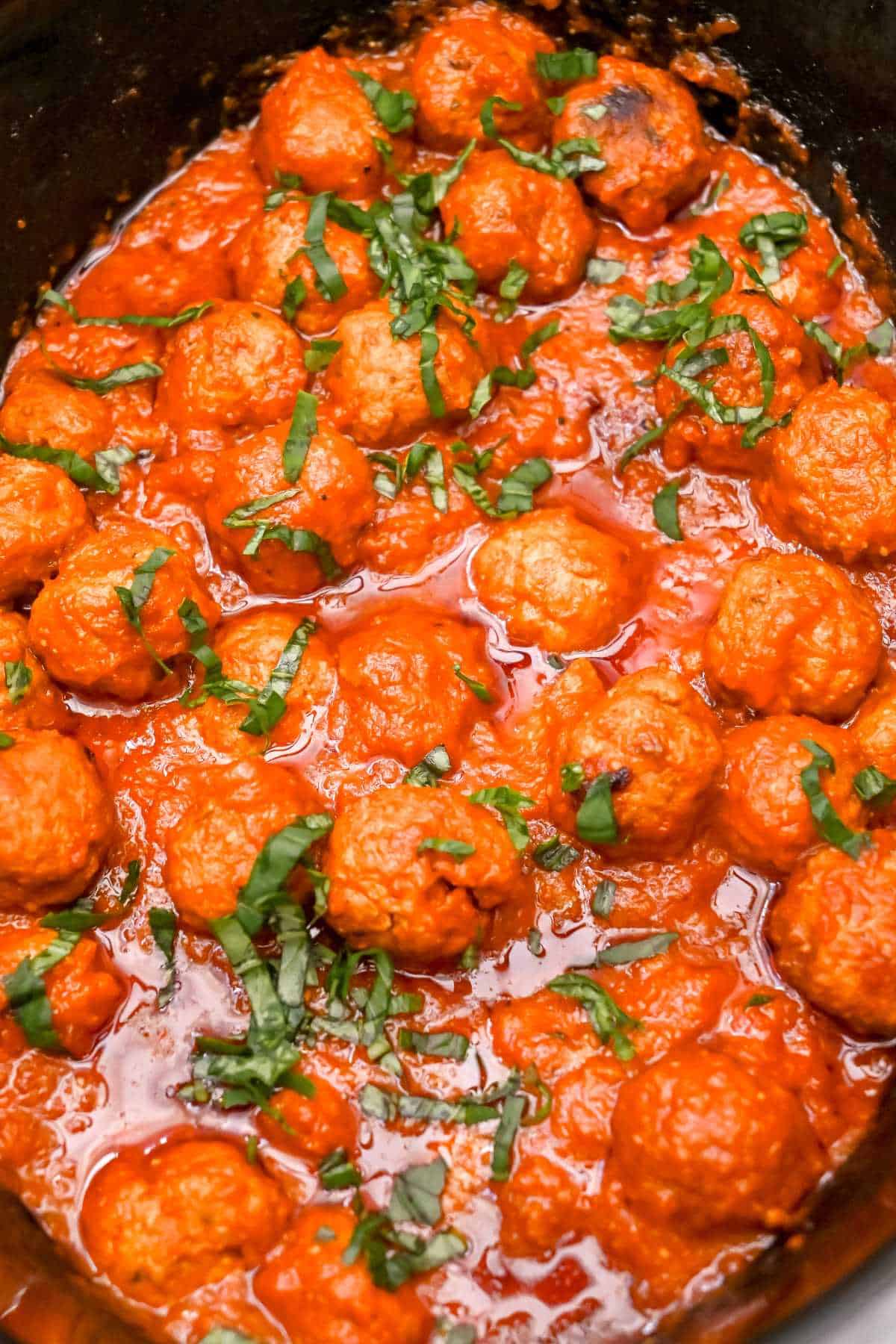 cooked turkey meatballs in a crock pot covered with sauce and topped with basil.