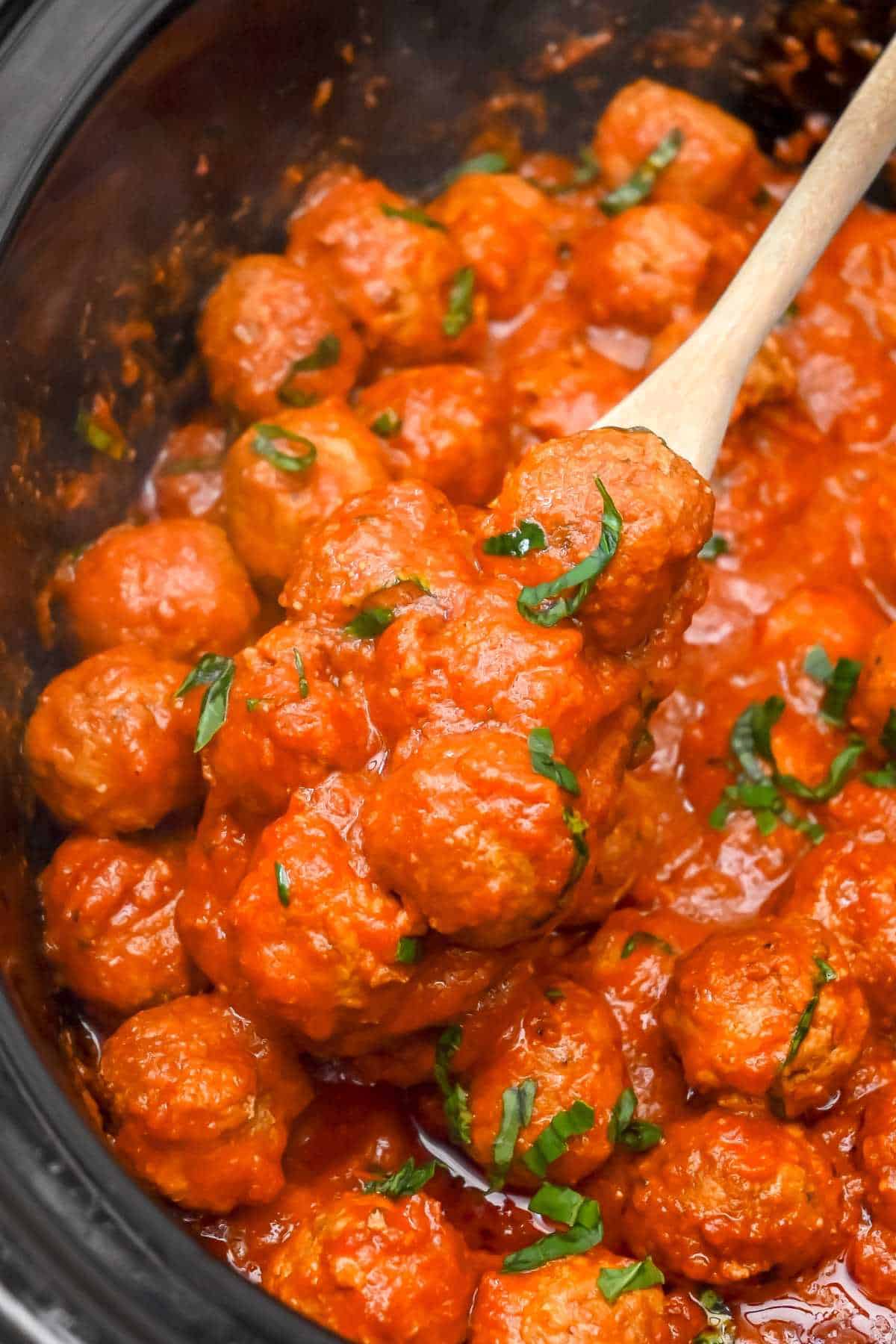 cooked turkey meatballs in sauce in a slow cooker with a wooden spoon.