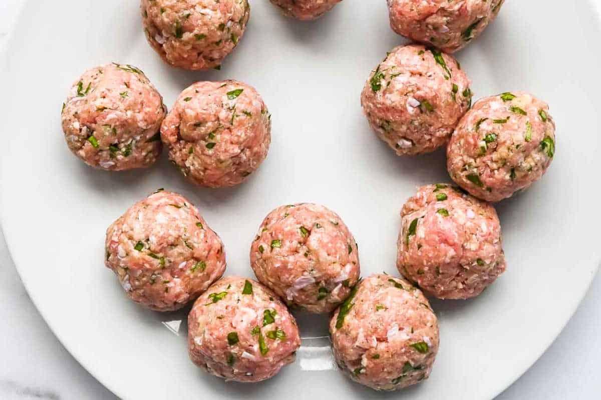 uncooked meatballs on a white plate.