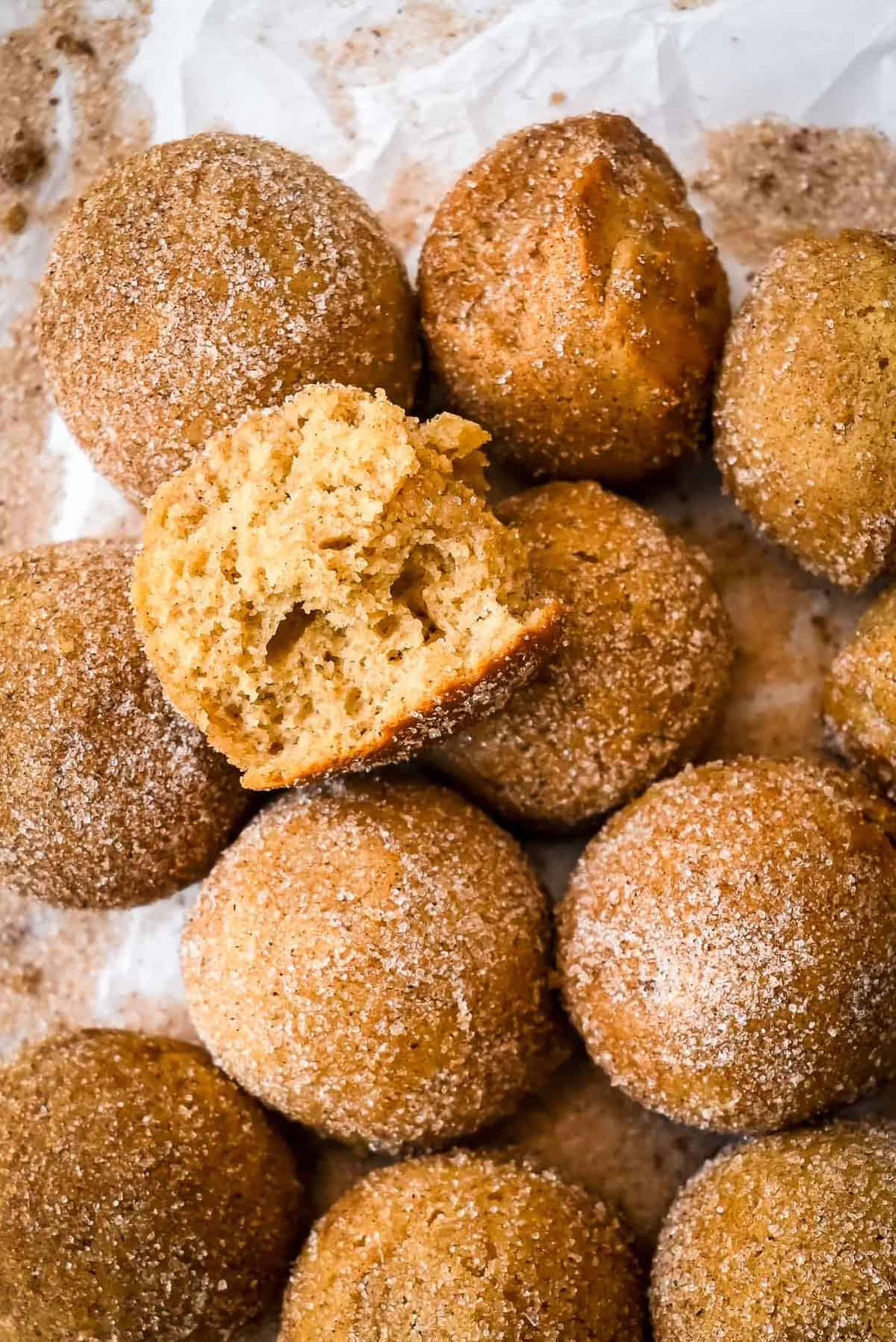 bite shot of apple cider donut holes in a pile on white parchment paper with cinnamon sugar.