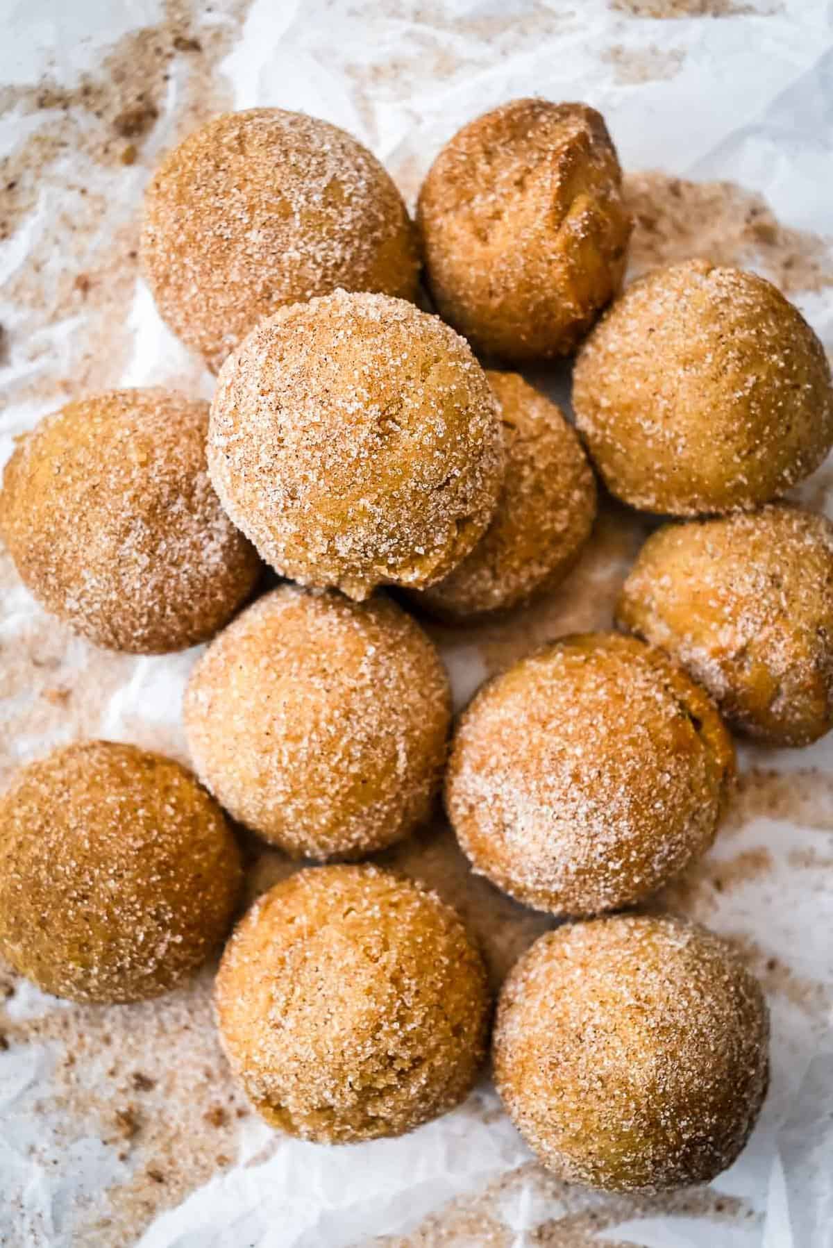 apple cider donut holes in a pile on white parchment paper with cinnamon sugar.