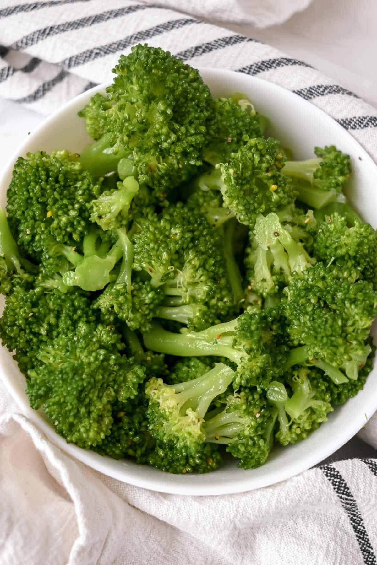 bowl of steamed broccoli in a white bowl on top of a blue and white striped towel.