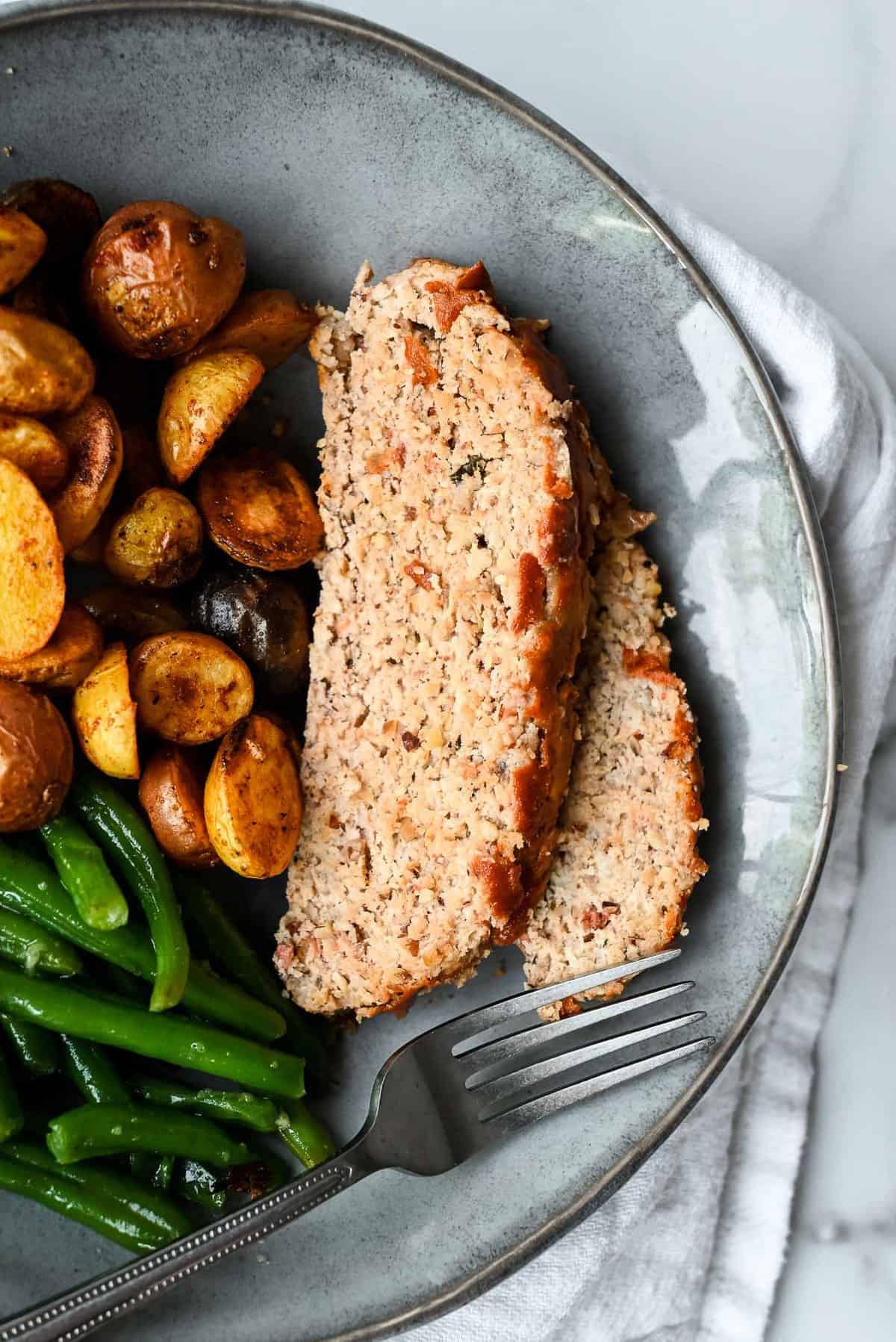 slices of chicken meatloaf without breadcrumbs on a plate with potatoes and green beans