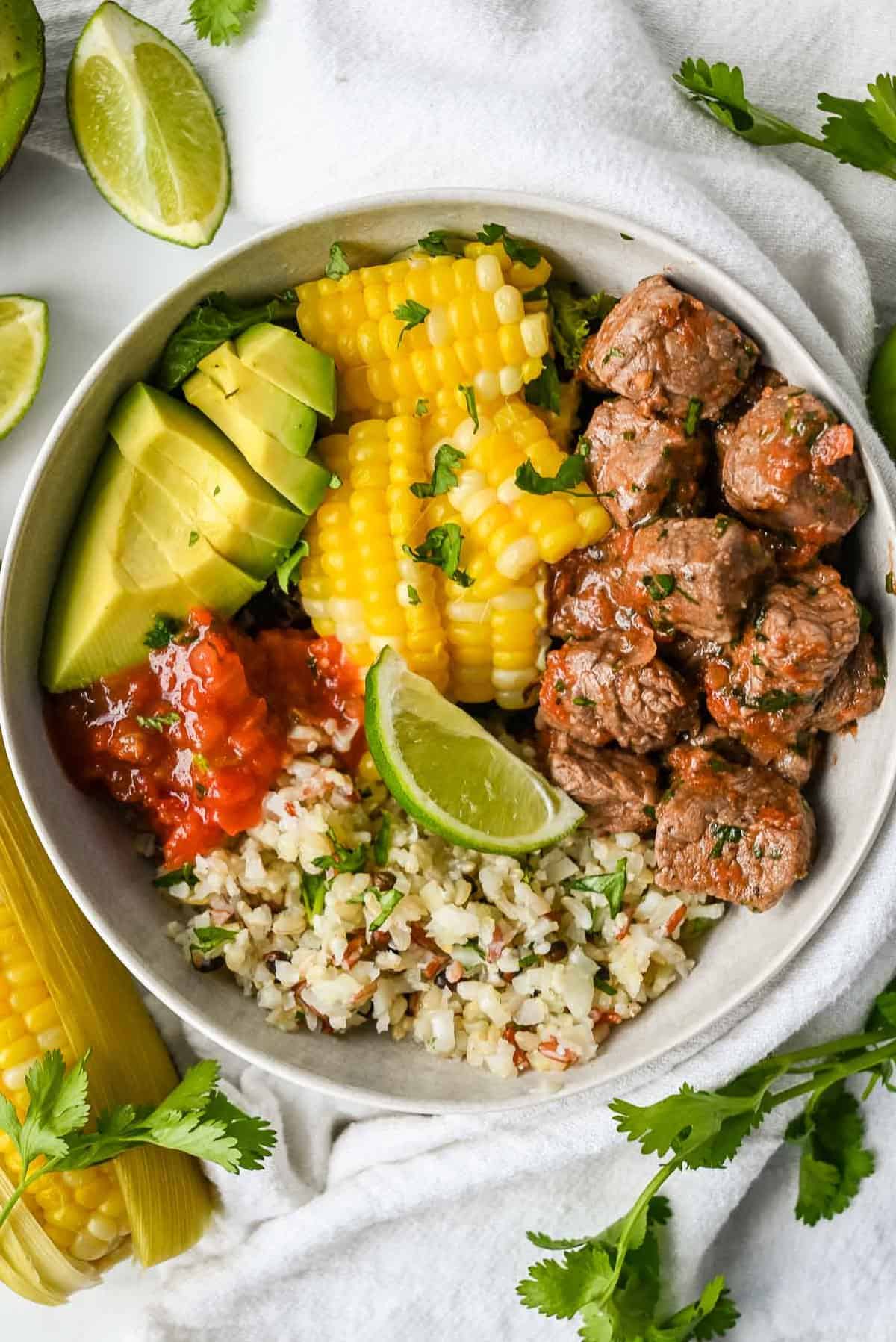 carne asada steak bowl with rice, corn, tomatoes, lime and avocado