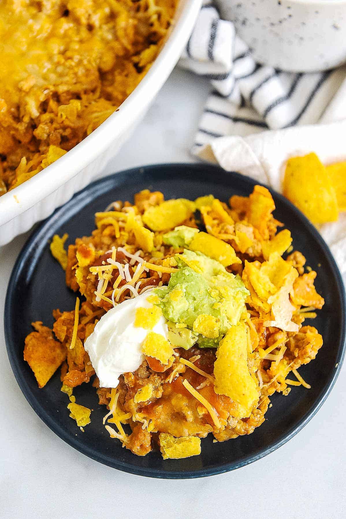 walking taco casserole topped with guacamole, sour cream, chips and cheese.