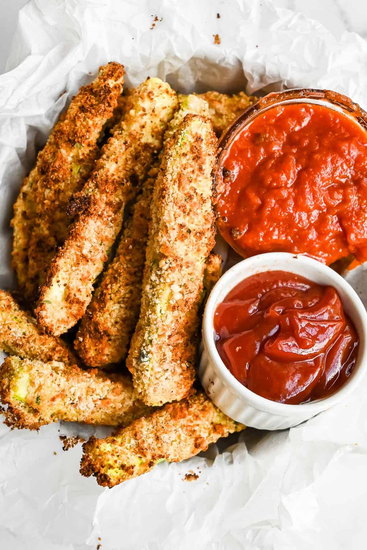 air fryer zucchini fries in a bowl with marinara and ketchup dipping sauces