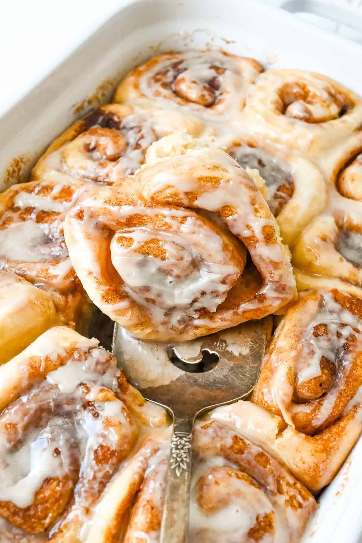 pan of dairy free cinnamon rolls with one roll on top.