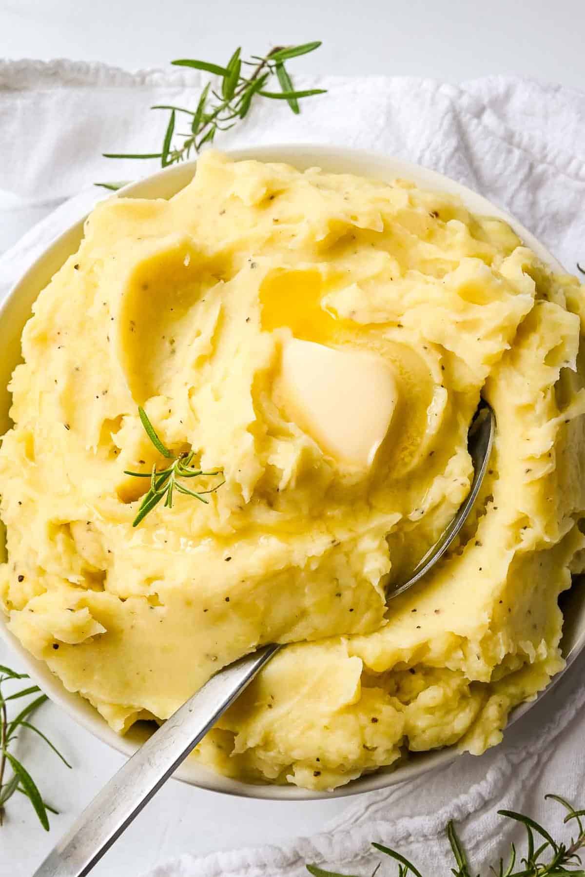 dairy free mashed potatoes topped with butter and a spoon in a white bowl.