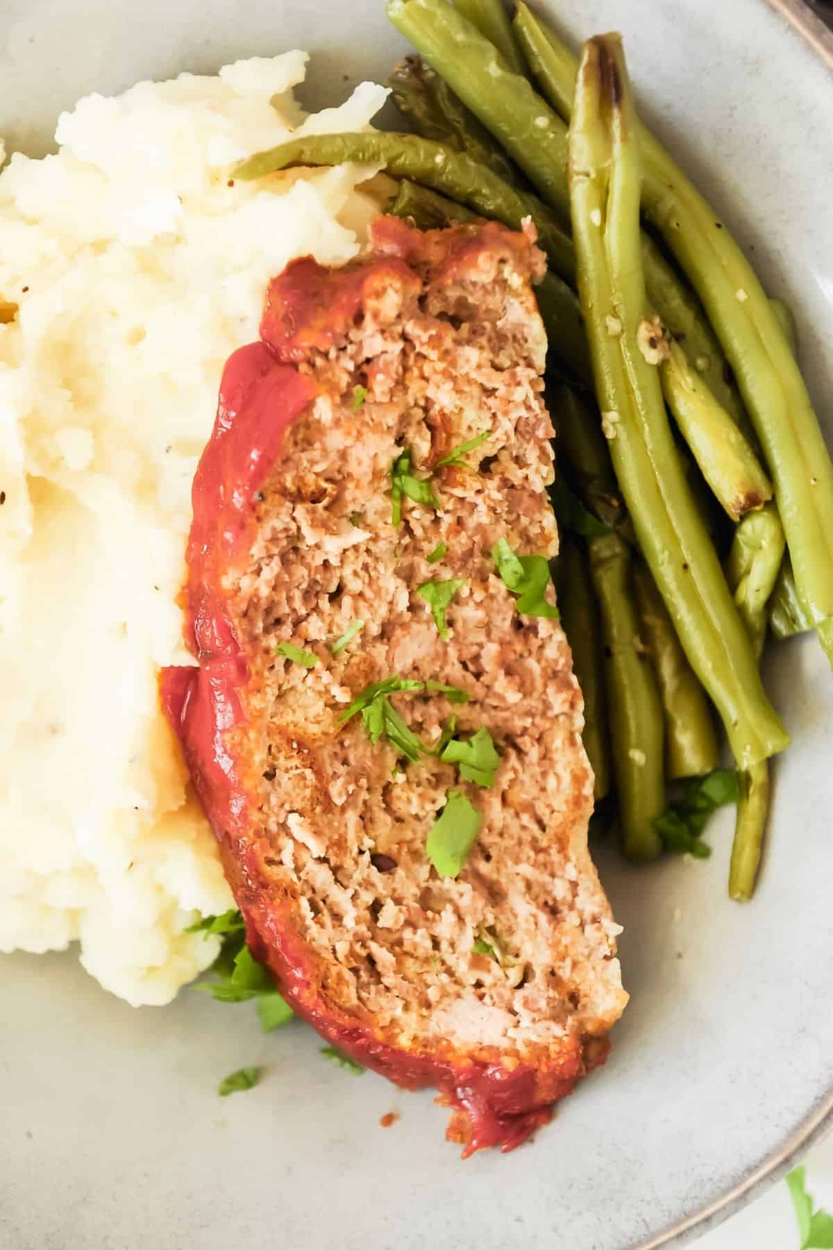 ranch meatloaf on a plate with green beans and mashed potatoes