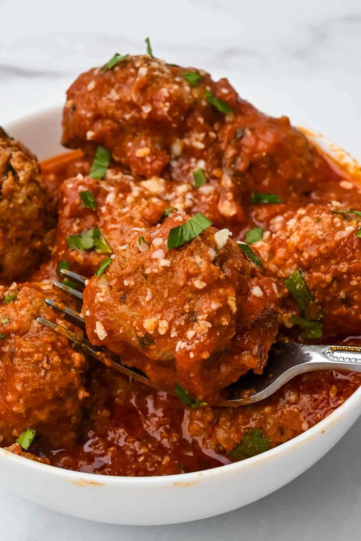 bowl of instant pot turkey meatballs with marinara sauce topped with parmesan cheese and parsley with fork under one meatball.