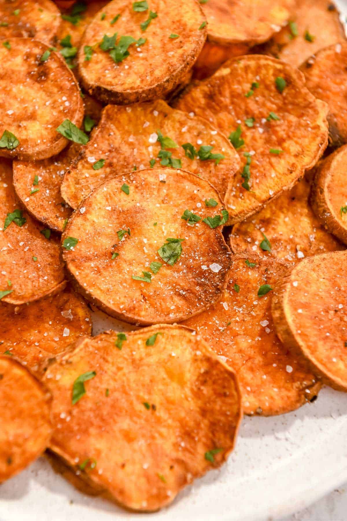 close up photo of air fryer sweet potato rounds in a pile topped with parsley and salt.