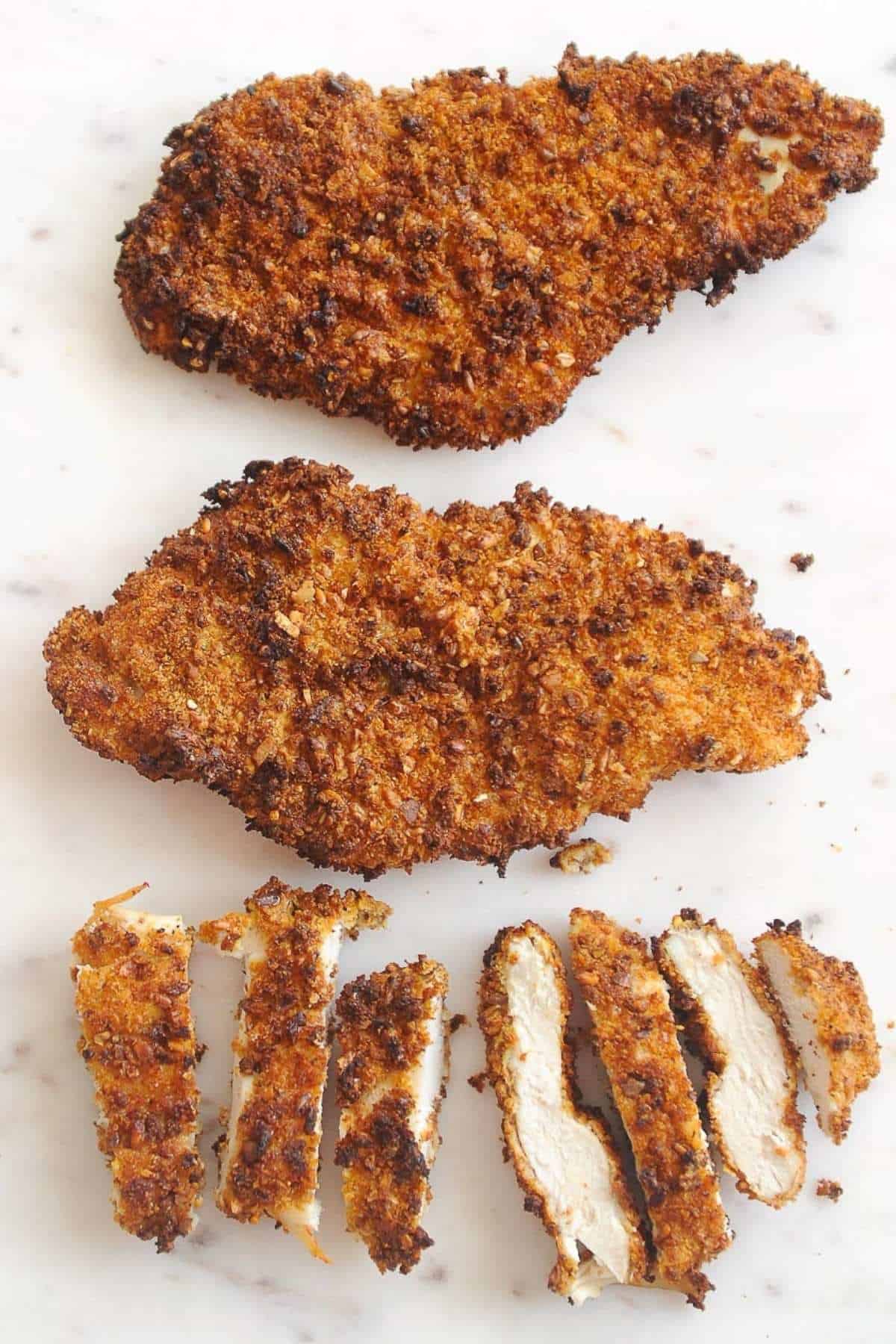 plate of air fried chicken cutlets on a marble slab with one cut into strips.
