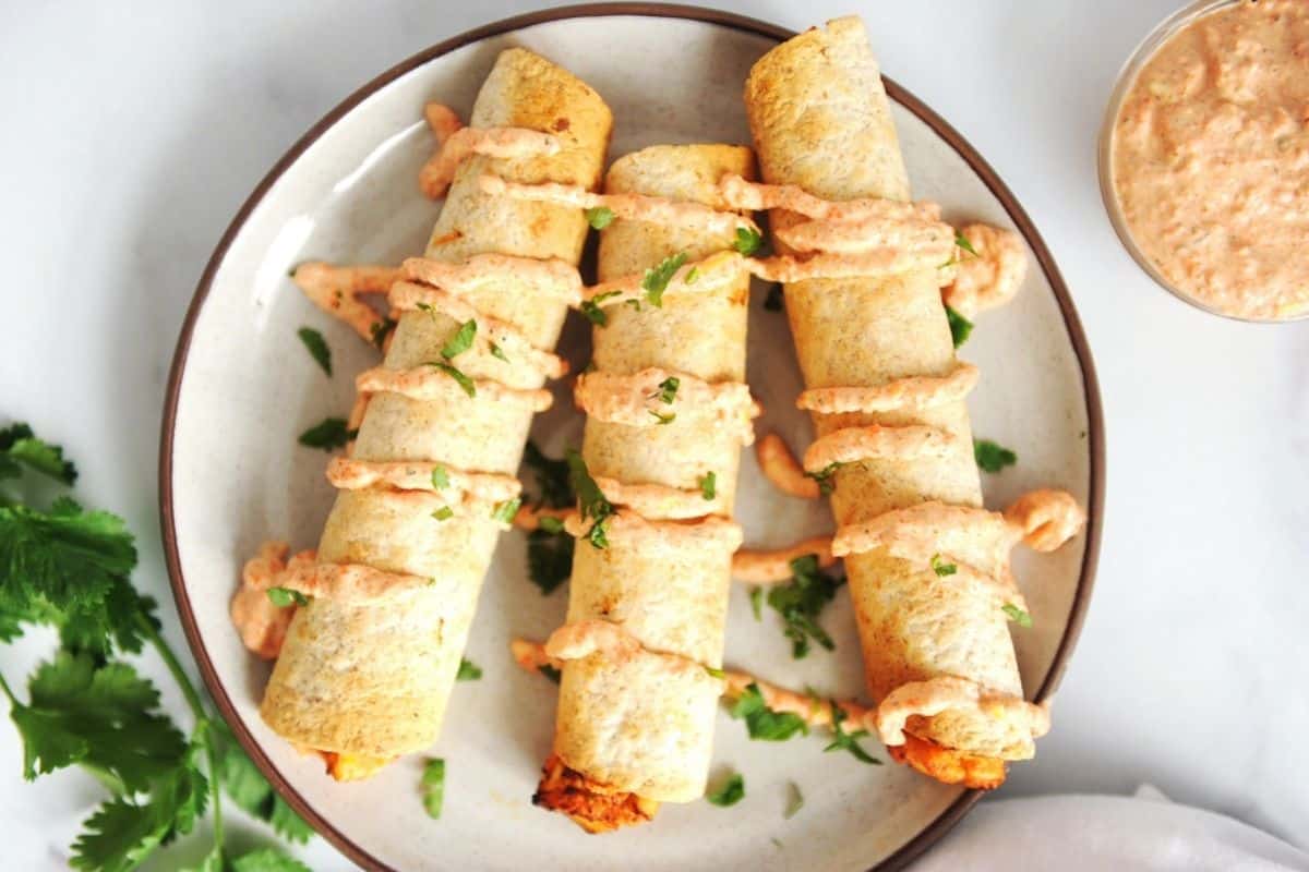plate of chicken taquitos with salsa drizzle and cilantro.