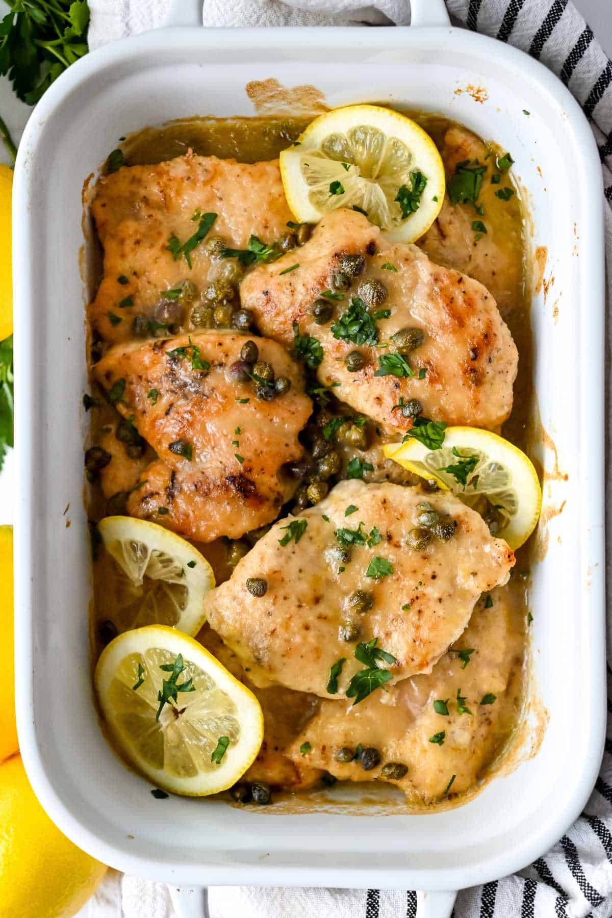 pan of chicken piccata topped with parsley and lemons.