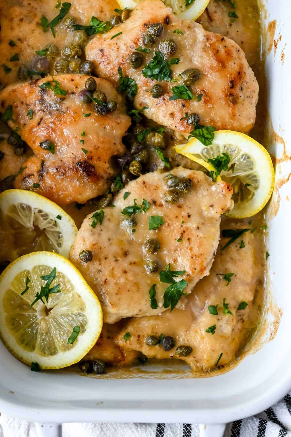 up close shot of chicken piccata topped with parsley, capers and lemons.