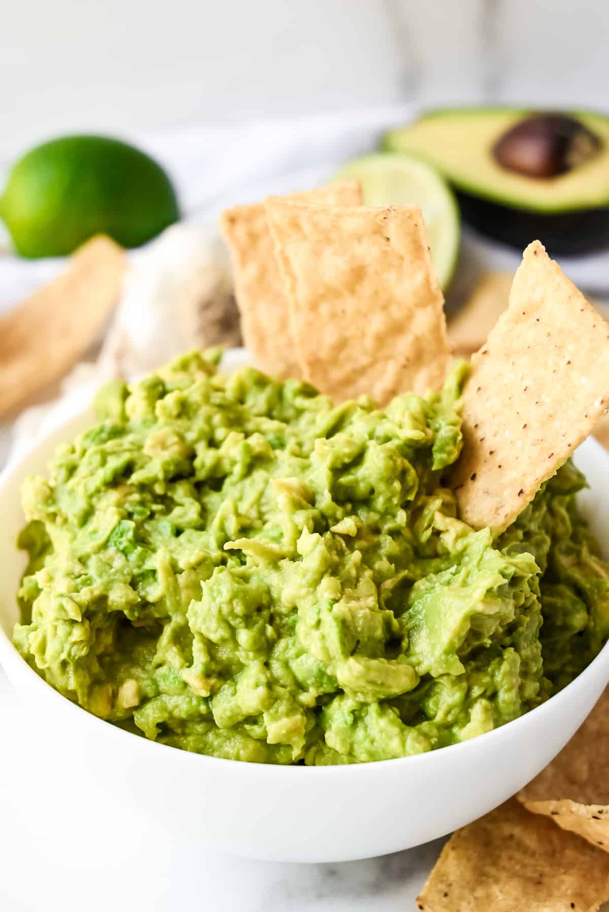 bowl of creamy simple guacamole in a white bowl with tortilla chips.