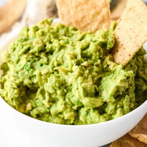 guacamole in a white bowl with two tortilla chips.