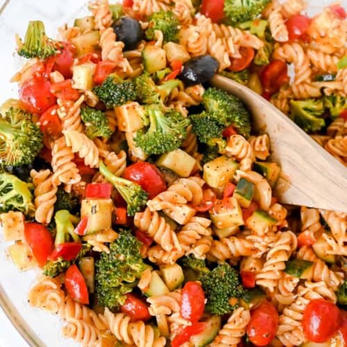 close up of gluten-free pasta salad with vegetables and a wooden spoon in a glass bowl.