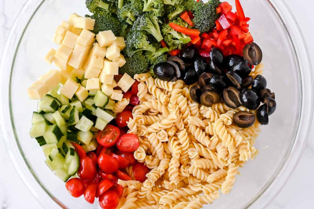 gluten-free pasta salad ingredients in a glass bowl on a white background.