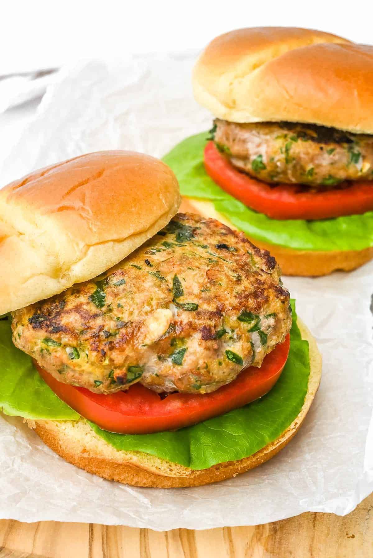 two turkey burgers on a piece of parchment paper with one bun offset to show patty.