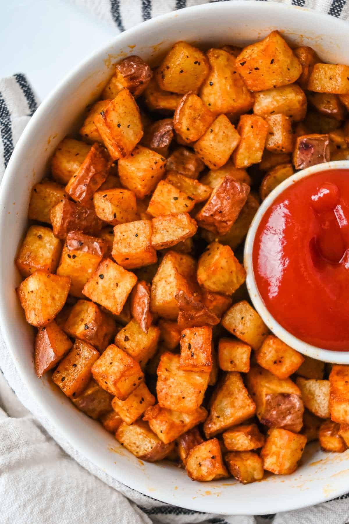 air fryer red potatoes in a white bowl with a side of ketchup.