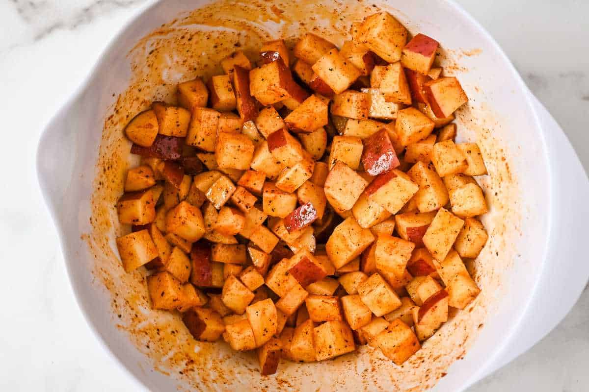 potatoes mixed with seasoning in a white bowl.