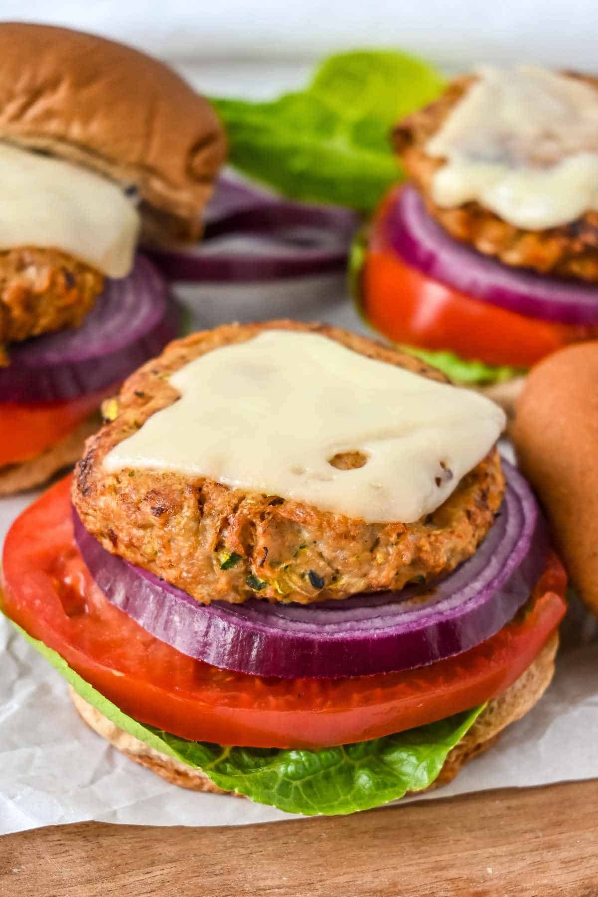 close up shot of air fryer turkey burgers topped with swiss cheese and with a bun on the side, lettuce, tomato, and onion.