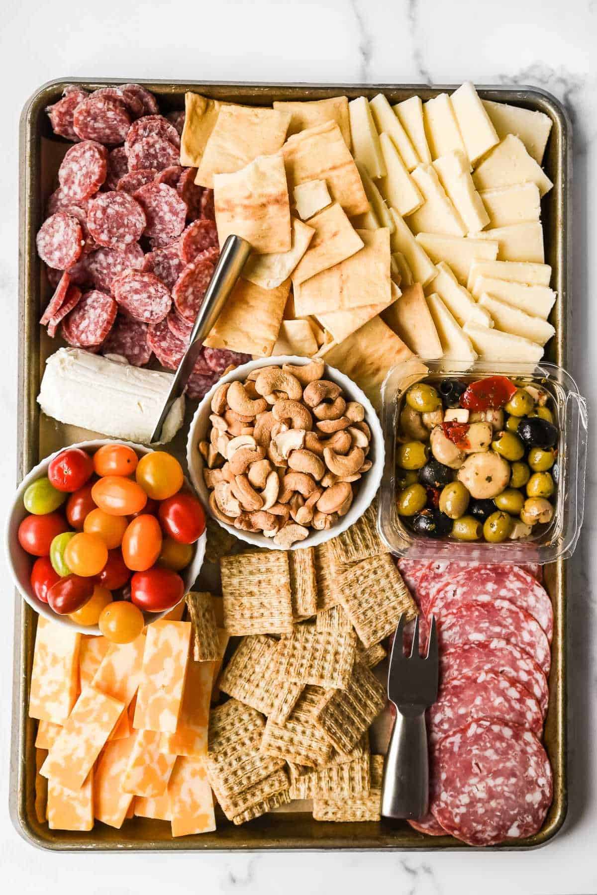 large aldi charcuterie board on a sheet pan with crackers, meats, cheeses, nuts, olives, and tomatoes.