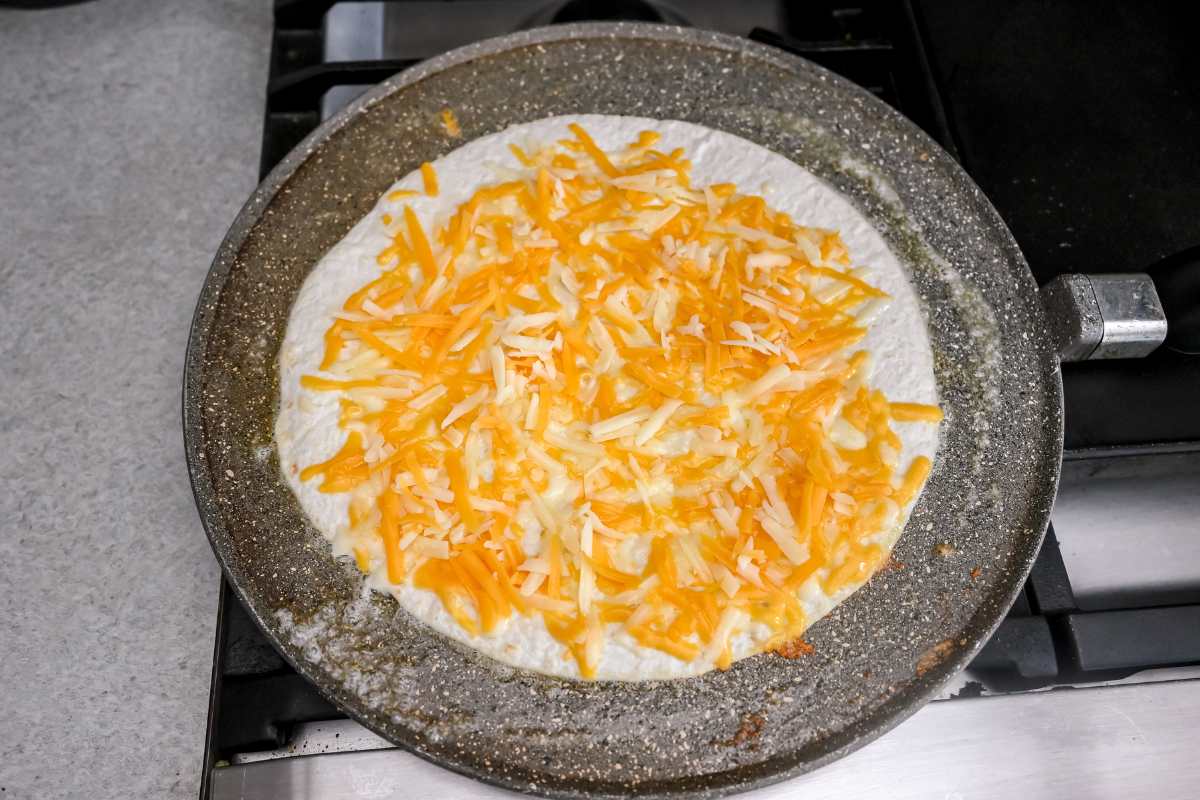 melted cheese on a tortilla on a gray pan on the stove.