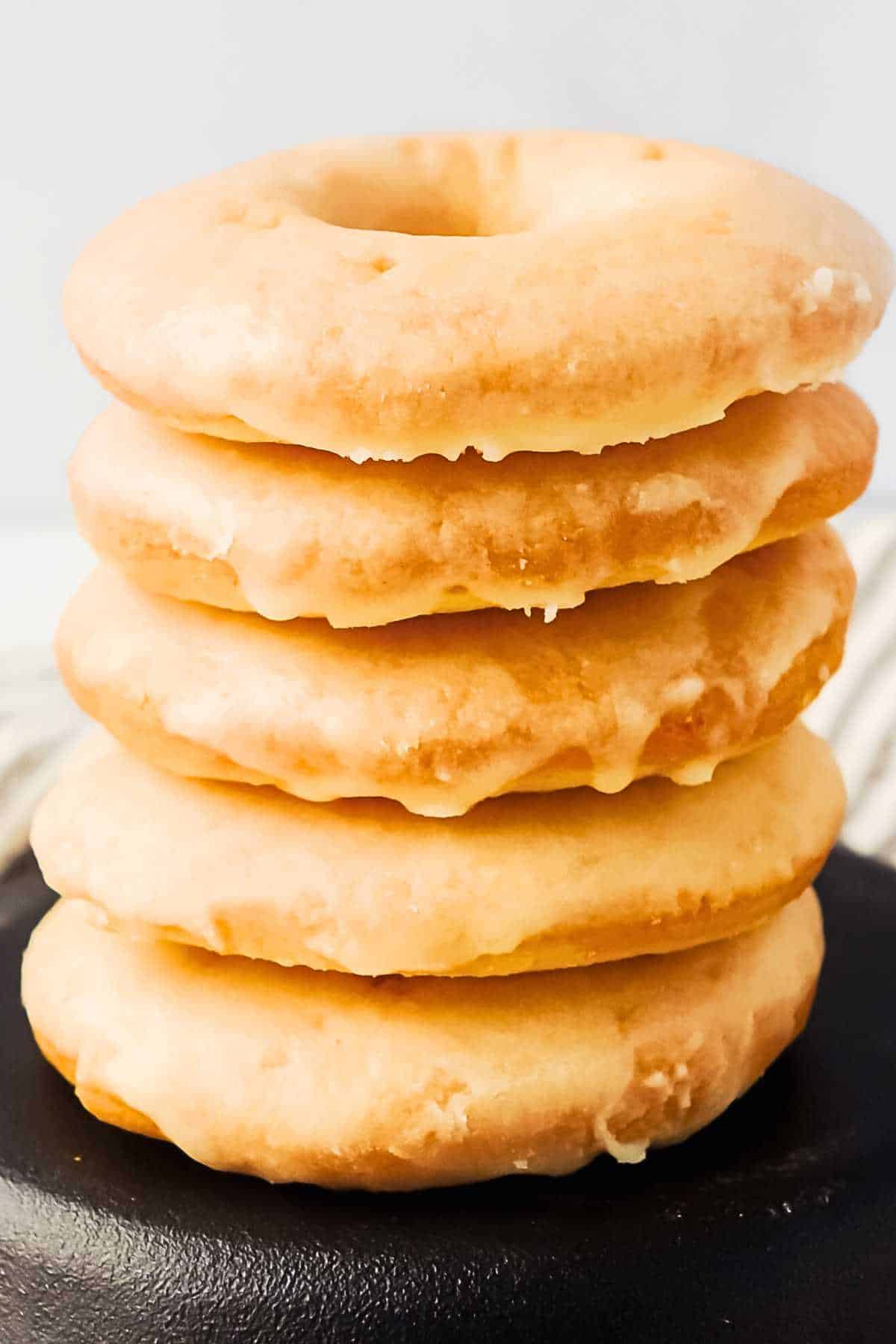 stack of keto donuts with glaze on a black plate.