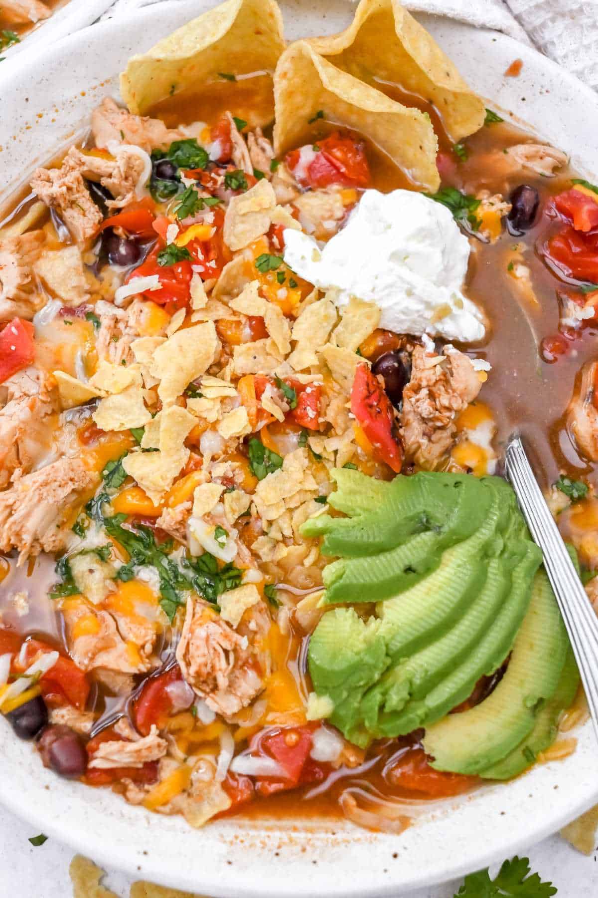 close up of 5-ingredient chicken tortilla soup in a white bowl topped with avocado and sour cream.