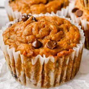 close up of pumpkin zucchini muffins in a white liner topped with chocolate chips.