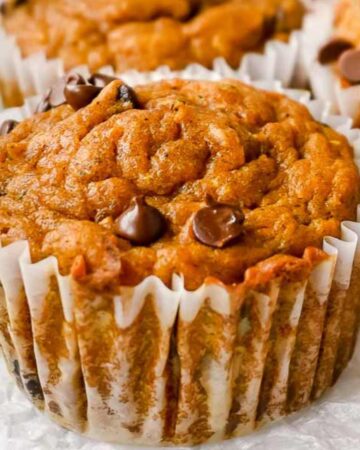 close up of pumpkin zucchini muffins in a white liner topped with chocolate chips.