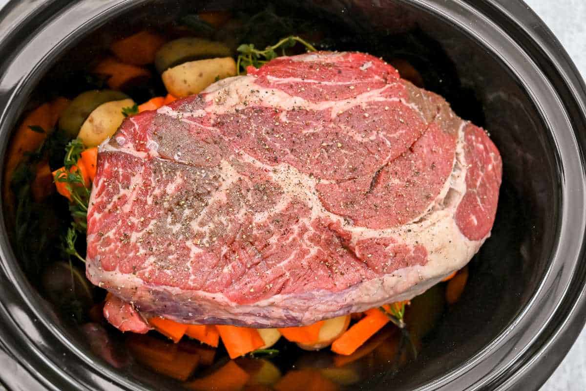 seasoned meat in a crock pot on top of vegetables.