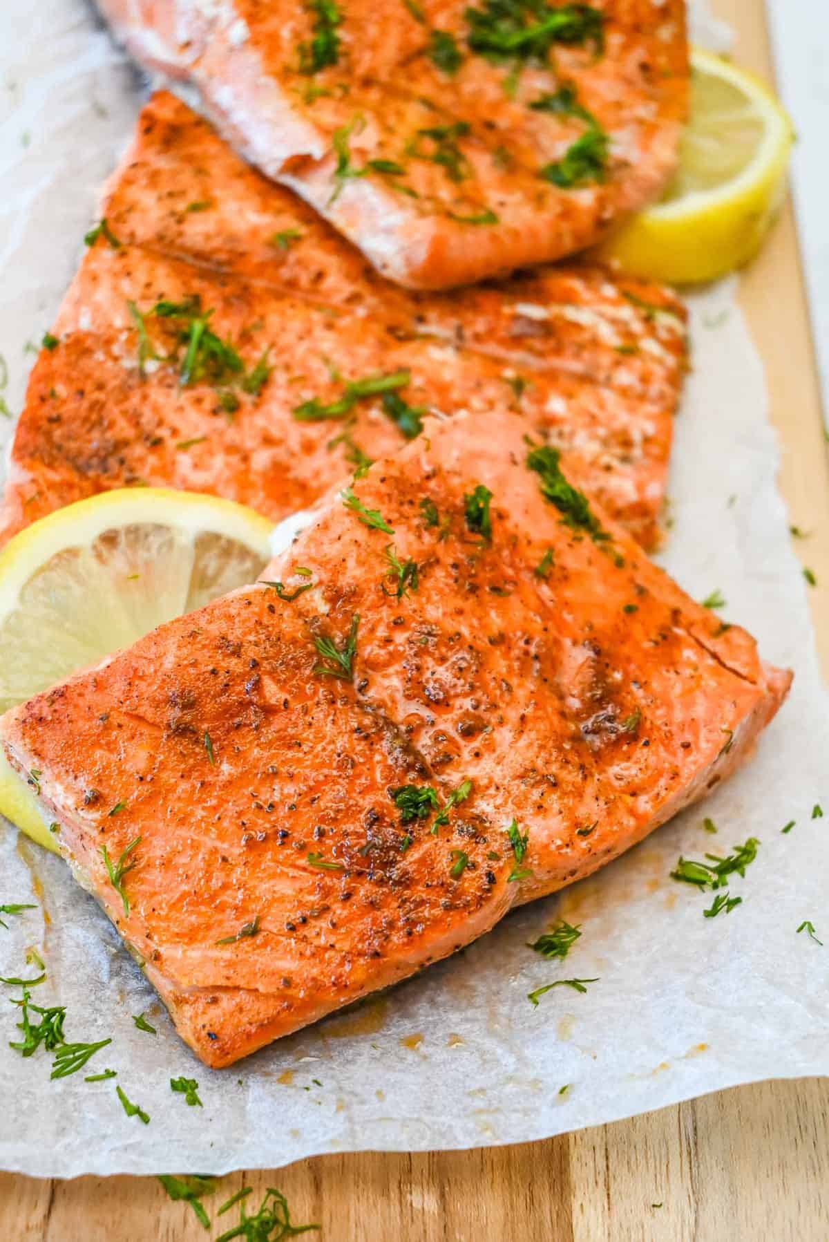 old bay salmon topped with dill and with lemon on parchment.