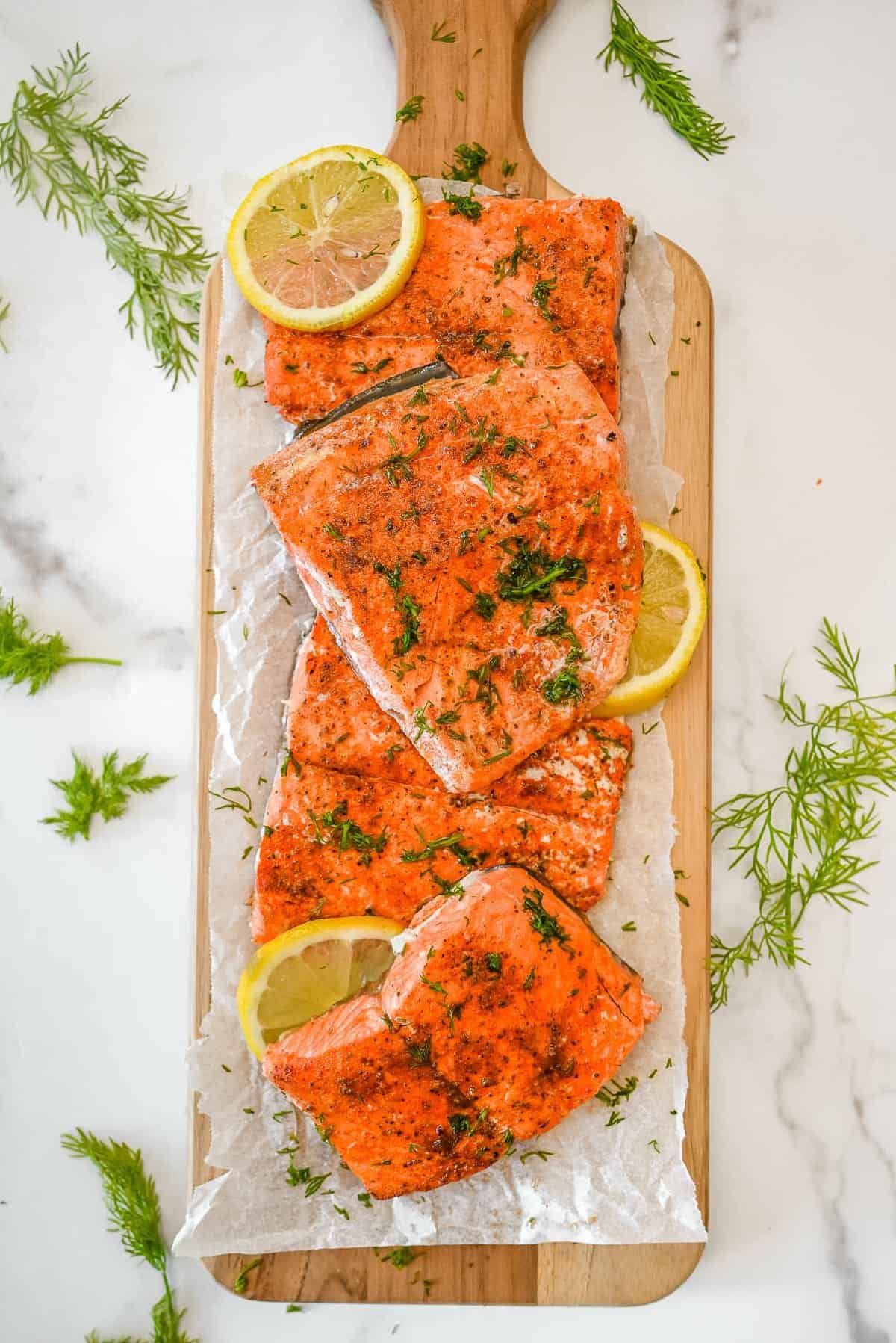 fillets of Old Bay Salmon on parchment paper with lemons and dill.