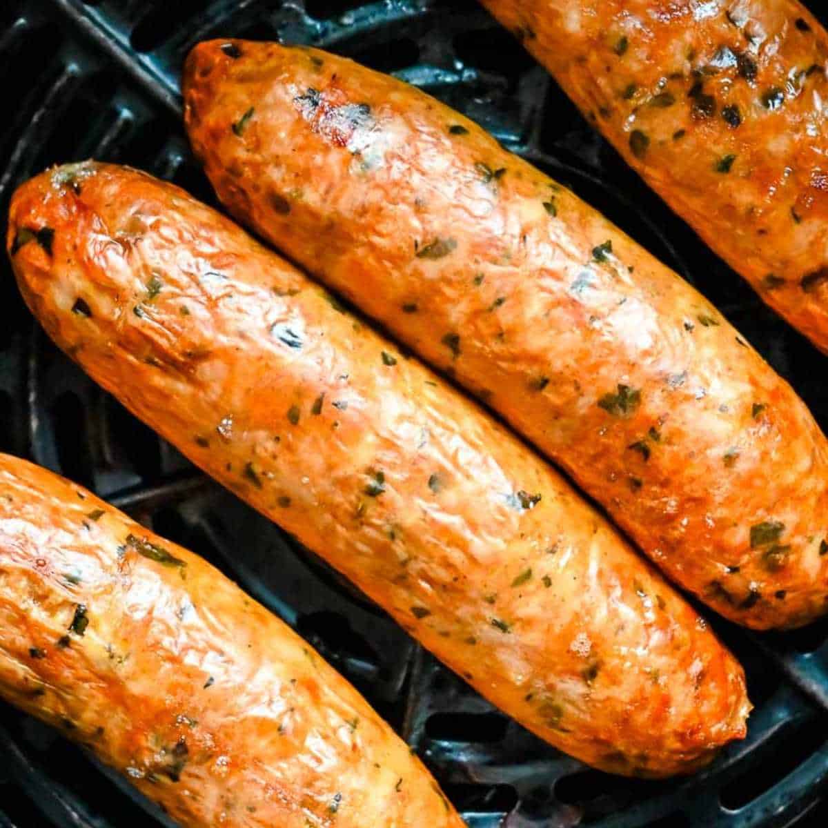 close up shot of air fryer chicken sausage in a black air fryer basket.