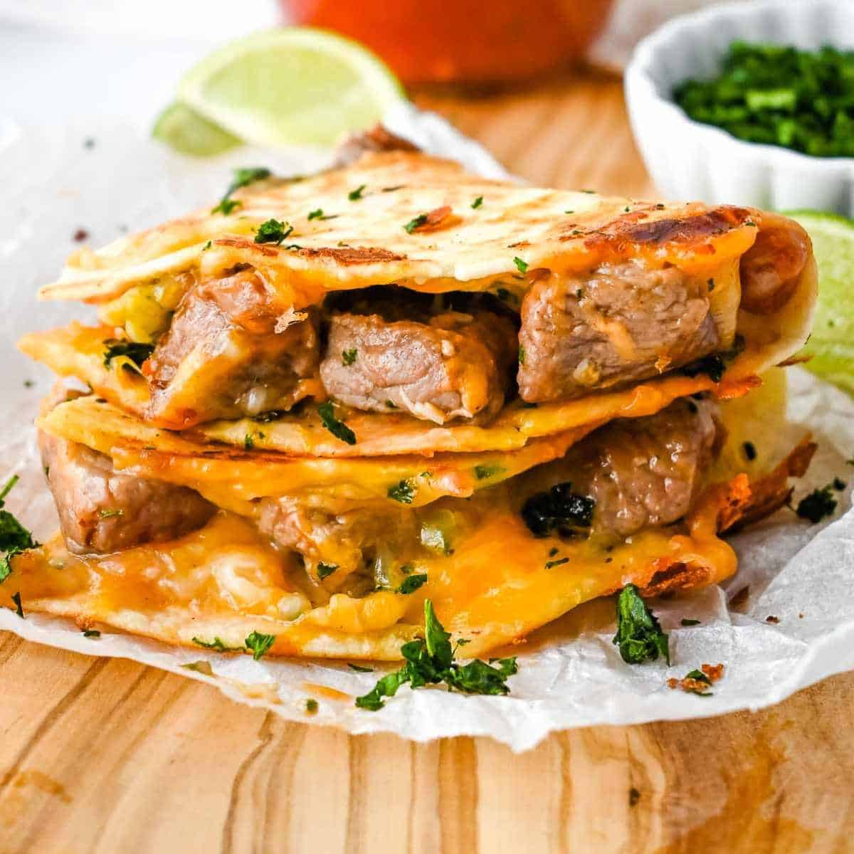 stack of carne asada quesadilla pieces on a wooden board.